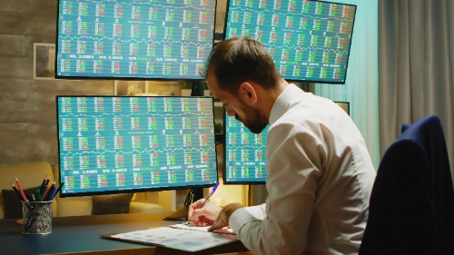 Hombre tomando notas mientras revisa el mercado bursátil desde su oficina en casa, elaborando su plan de trading