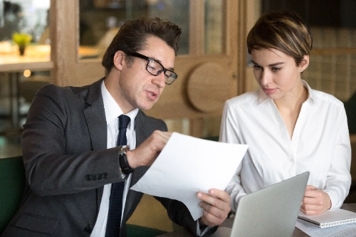 Hombre de negocios consultando las condiciones de un contrato con una colega, representando la revisión de la regulación de un bróker