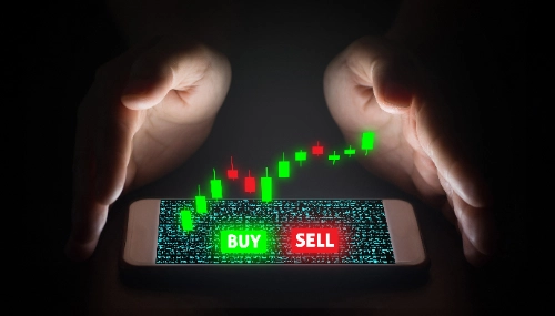 Dos manos rodean un teléfono sobre el que flota un gráfico de velas verdes y rojas con los botones BUY y SELL.