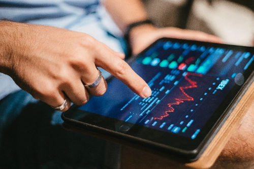 Un hombre usa su dedo para revisar gráficos financieros y datos del mercado bursátil en una tableta.