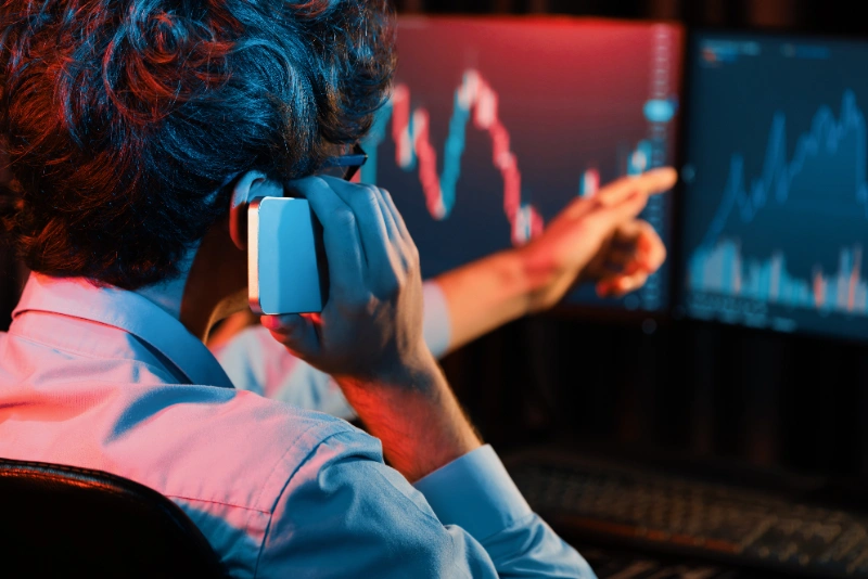 Joven inversor revisando datos de mercado en su teléfono y computadora