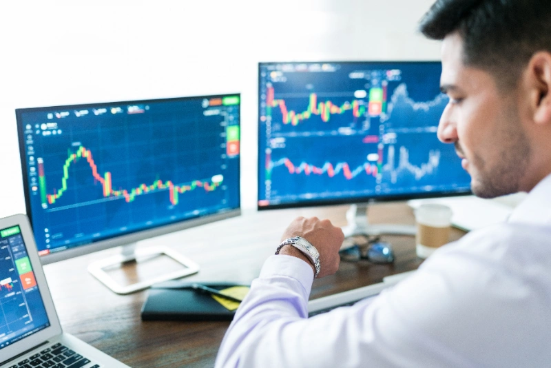 Broker confiado esperando la apertura del mercado mirando su reloj frente a la computadora