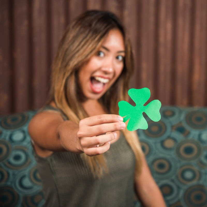 Mujer emocionada sosteniendo un trébol de papel verde, ilustración de ventaja real o racha de suerte en trading